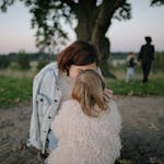 A tender moment between mother and daughter outdoors in a grassy field at twilight.