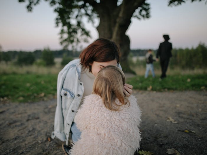 A tender moment between mother and daughter outdoors in a grassy field at twilight.